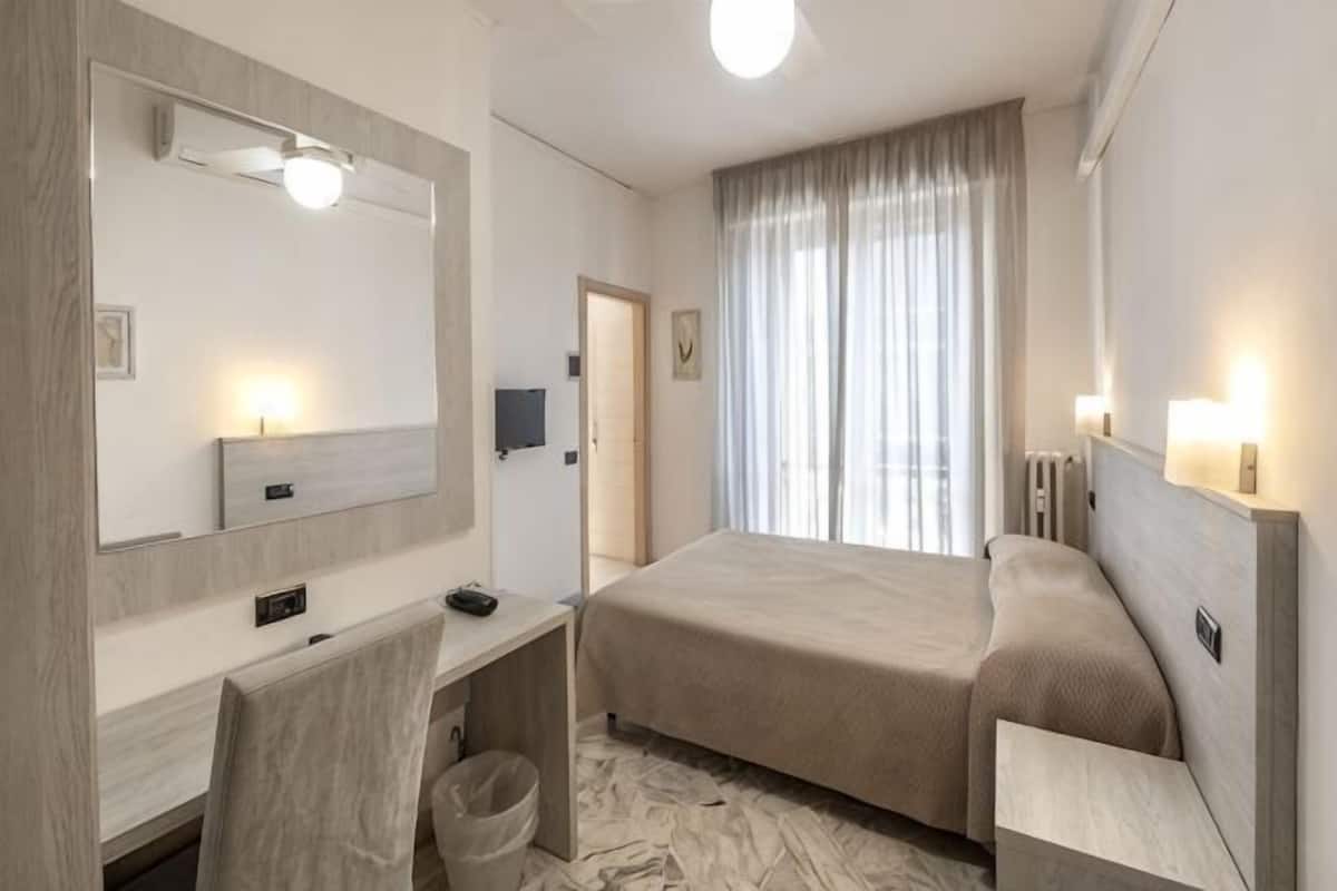 A hotel room with a bed, desk, chair, and a large mirror.