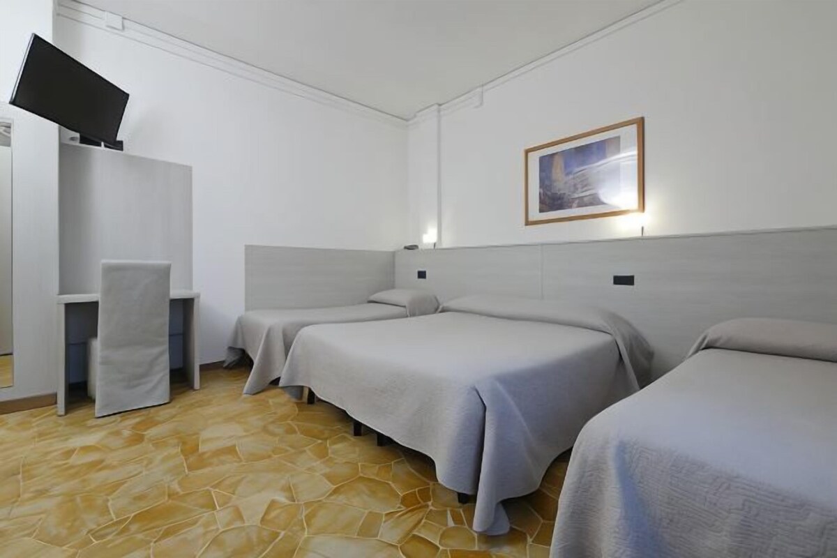 A hotel room with three beds, a TV on a stand, and a painting on the wall.