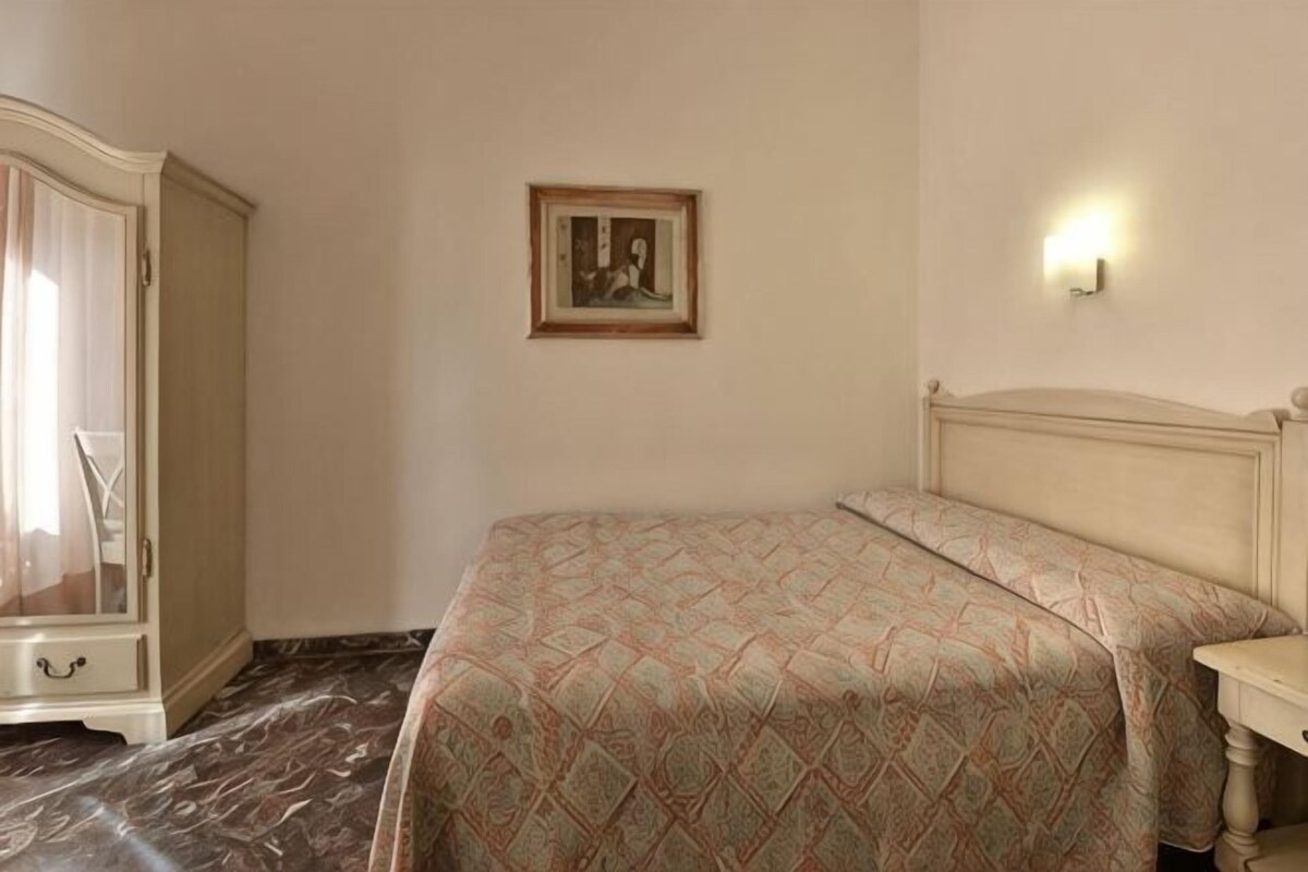 Een slaapkamer met een bed, een kledingkast, een schilderij aan de muur en een nachtkastje.