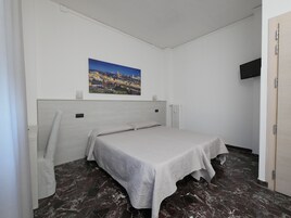 Una camera da letto con un letto, un comodino, una TV a parete, un quadro raffigurante un panorama urbano e un termosifone.