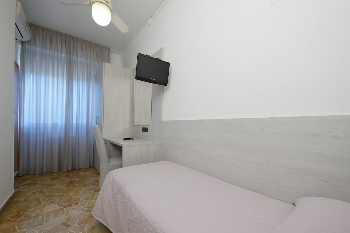 A hotel room with a bed, a desk, a chair, a television, and a window with curtains.