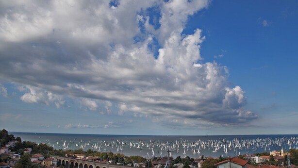 A coastal town with a marina filled with sailboats, a prominent arch bridge, and a clear blue sky with scattered clouds. - Greif Hotel & Spa Trieste  (Trieste)