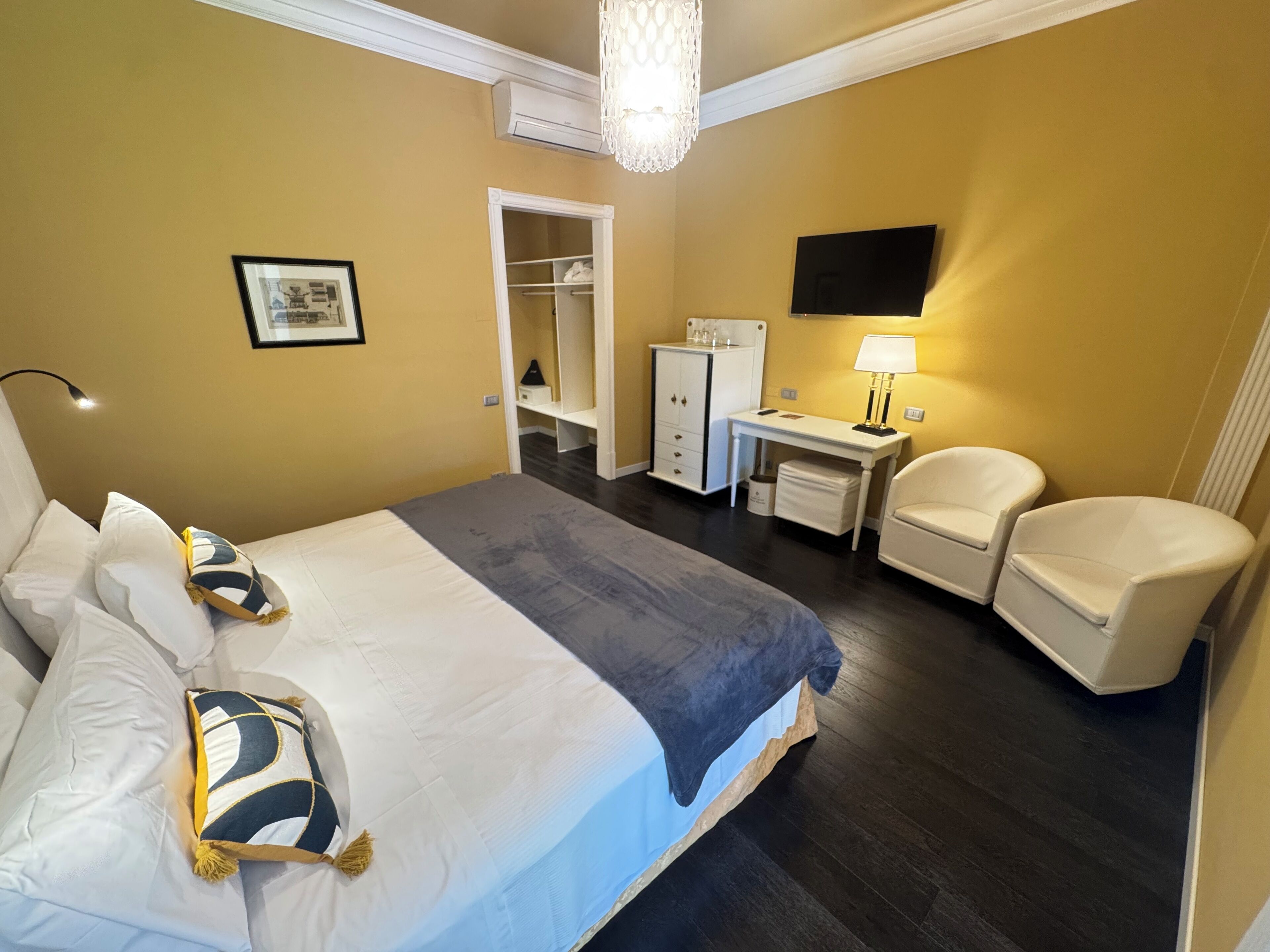 A hotel room with a large bed, a desk, a chair, a wardrobe, and a flat-screen TV.