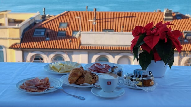 A table with breakfast items, a potted plant, and a view of the sea and buildings. - Greif Hotel & Spa Trieste  (Trieste)
