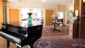 A grand piano in a spacious lobby with a patterned carpet, a vase with flowers, and a bust on a pedestal. - Greif Hotel & Spa Trieste  (Trieste)