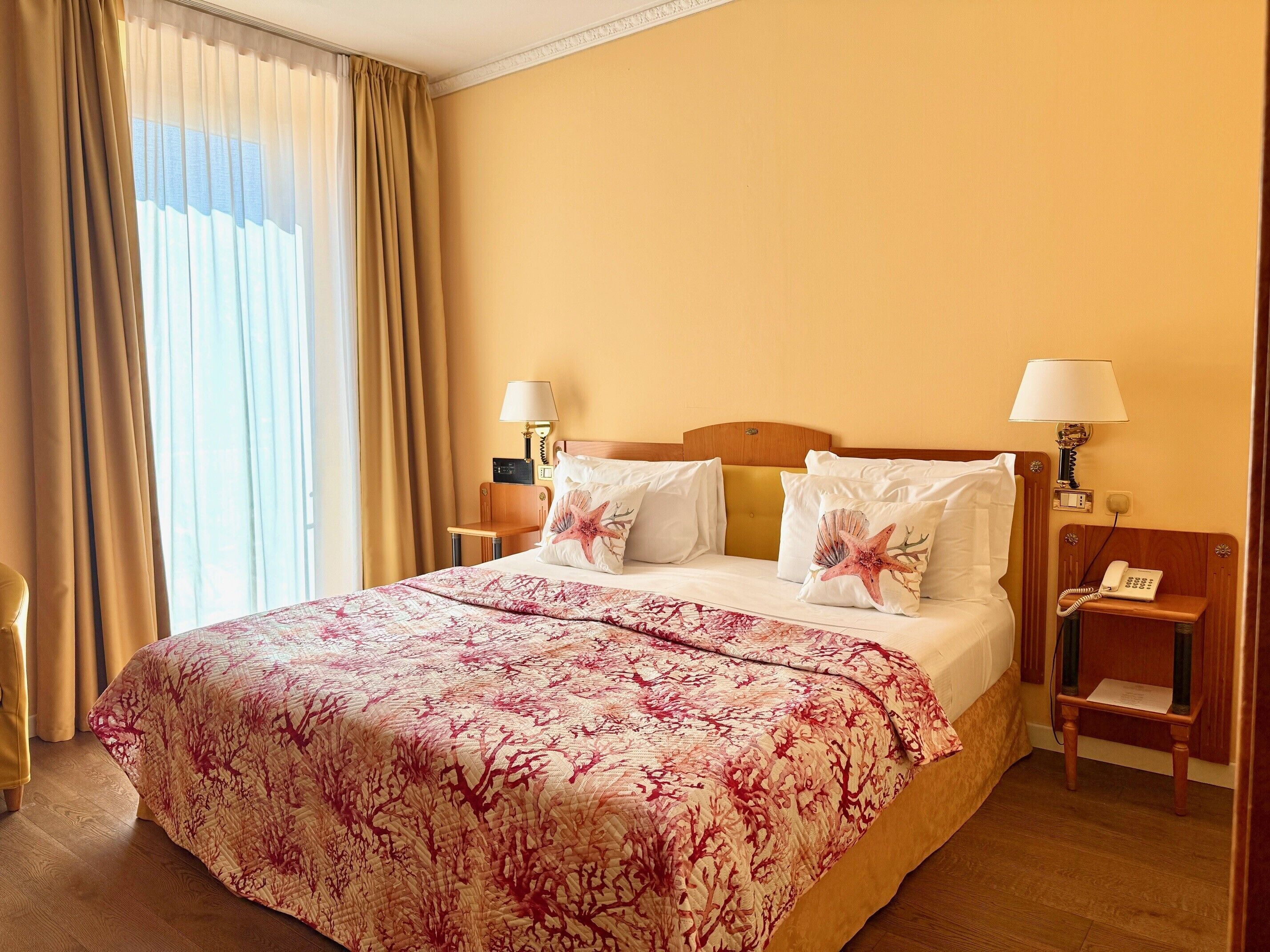 Une chambre d’hôtel avec un grand lit, deux lampes de chevet, une table de chevet avec un téléphone et une fenêtre avec des rideaux.