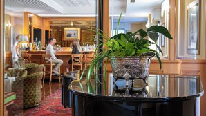 A bar area with a reflective black table, a decorative silver vase with green plants, and a patterned rug. - Greif Hotel & Spa Trieste  (Trieste)