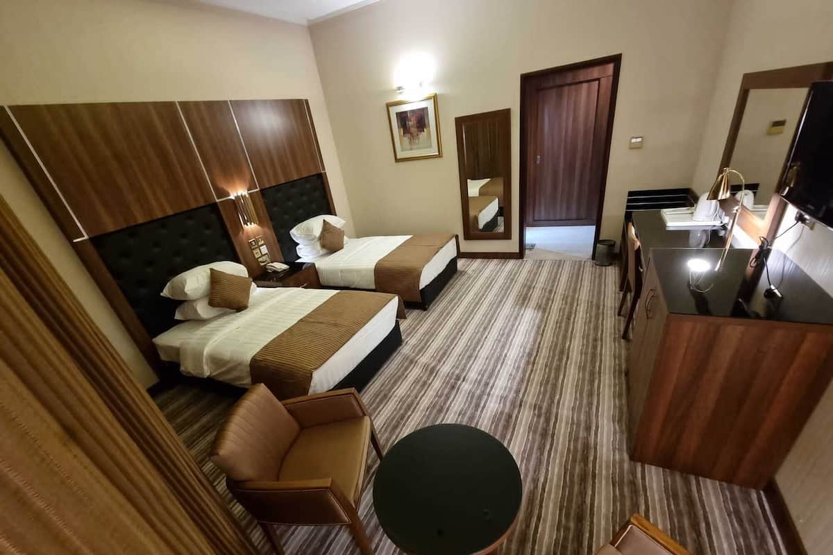 Quarto de hotel com duas camas, uma escrivaninha, uma cadeira e uma mesa redonda.
