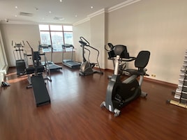 Un gimnasio espacioso con diferentes máquinas de cardio, una banca y una cinta de correr.