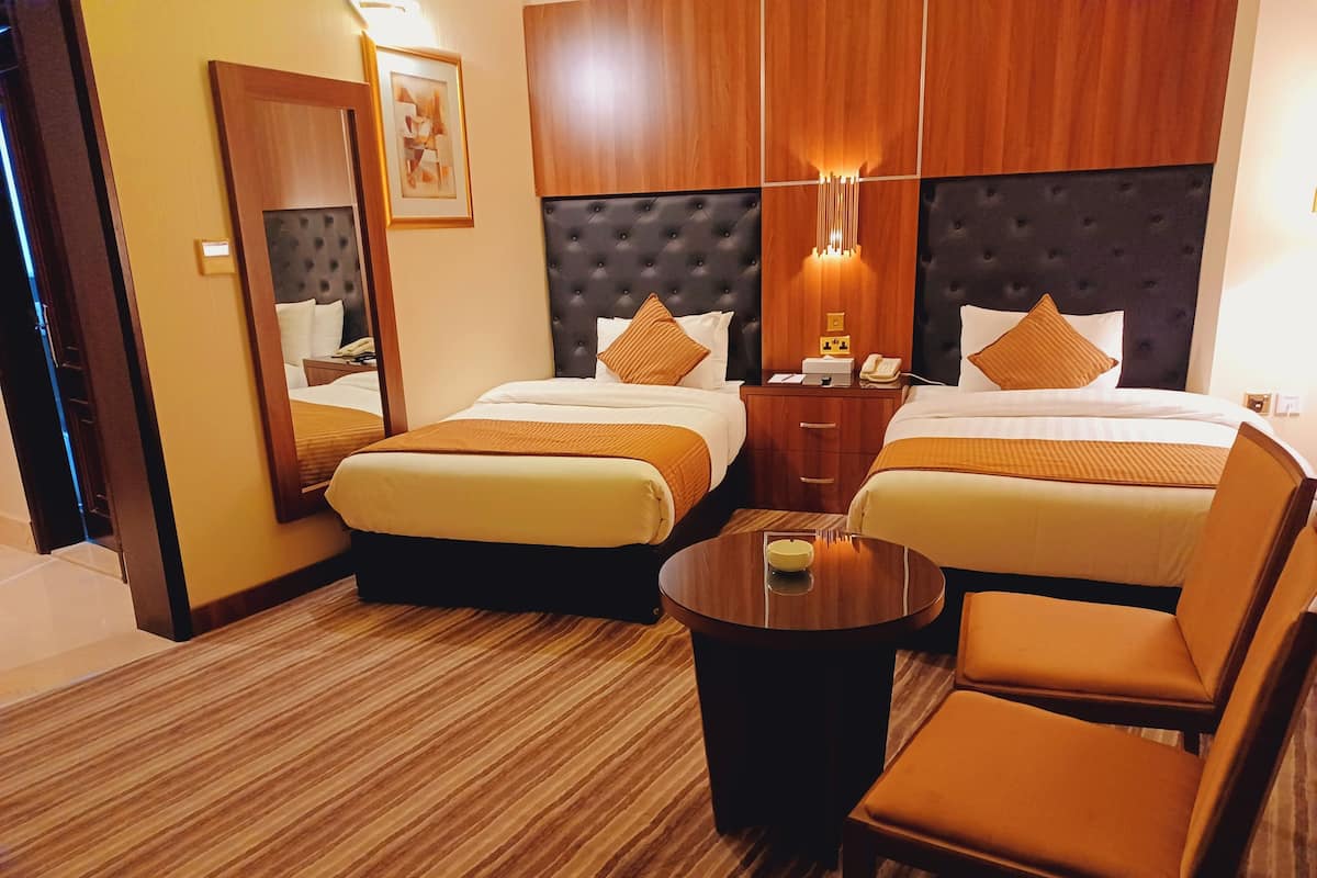 Quarto de hotel com duas camas, uma mesa de centro redonda e uma cadeira.