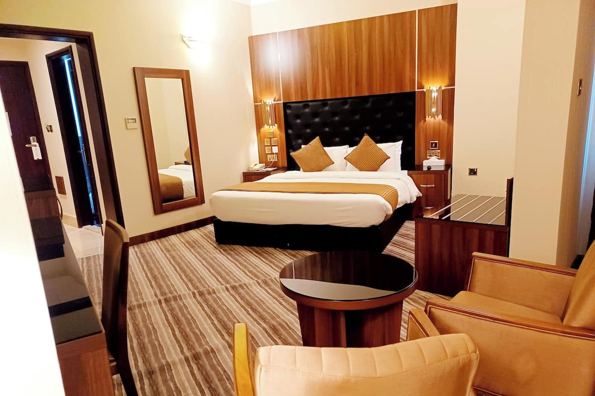 Quarto de hotel com uma cama grande, uma mesa de centro redonda, uma poltrona de couro e um espelho.