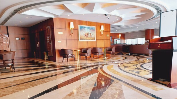 A spacious lobby with a marble floor, wooden paneling, and a large painting on the wall. - Royal Qatar Hotel (Doha)
