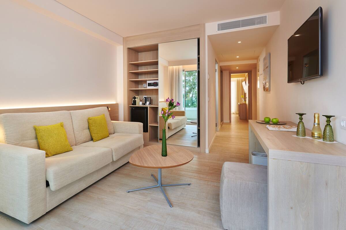 A modern living room with a sofa, a coffee table, and a kitchen area with a counter and two vases.