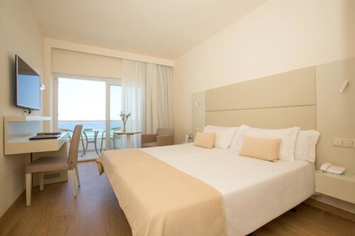 A hotel room with a large bed, a desk with a chair, a small table, and a TV mounted on the wall.