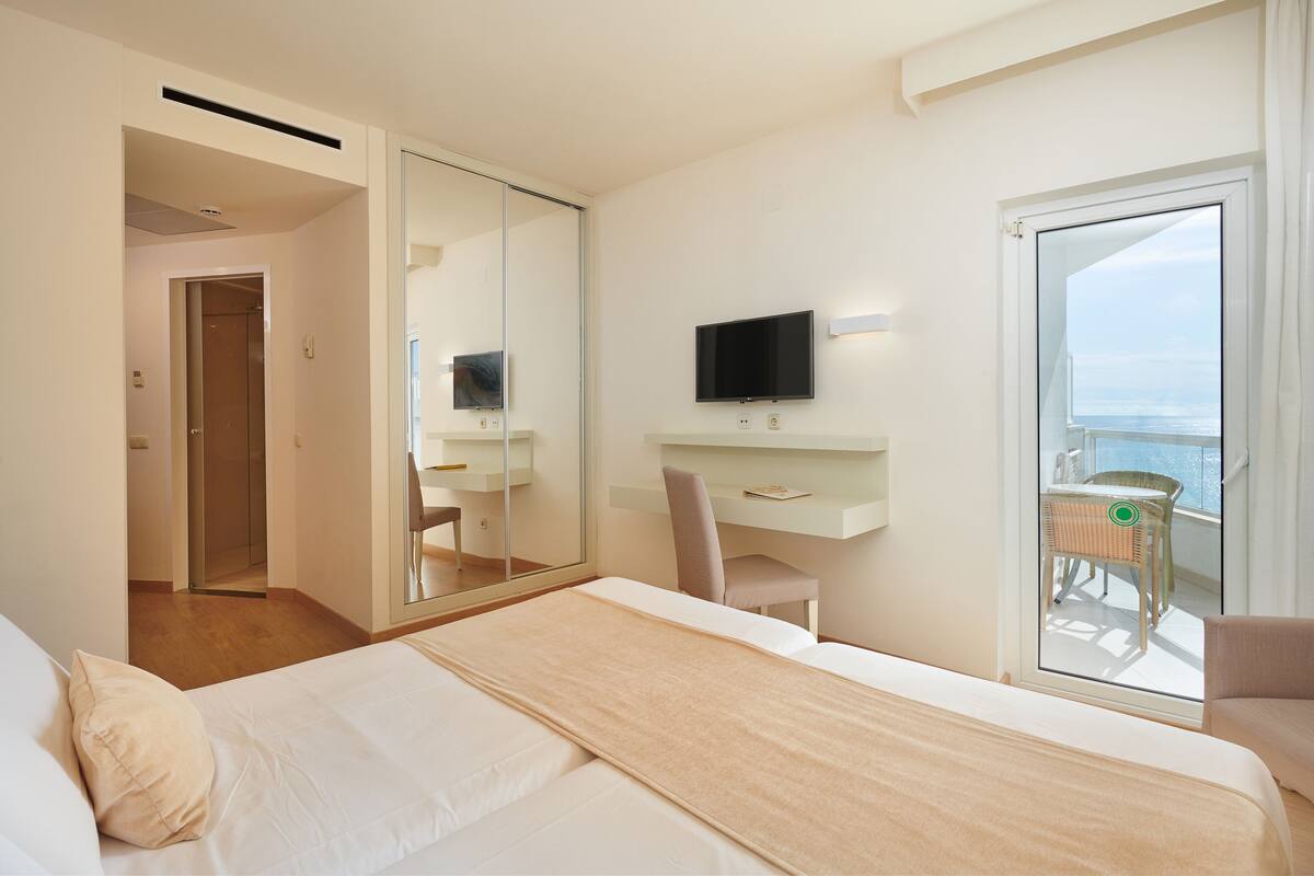 A hotel room with a bed, a desk, a chair, a TV, and a balcony with a view.