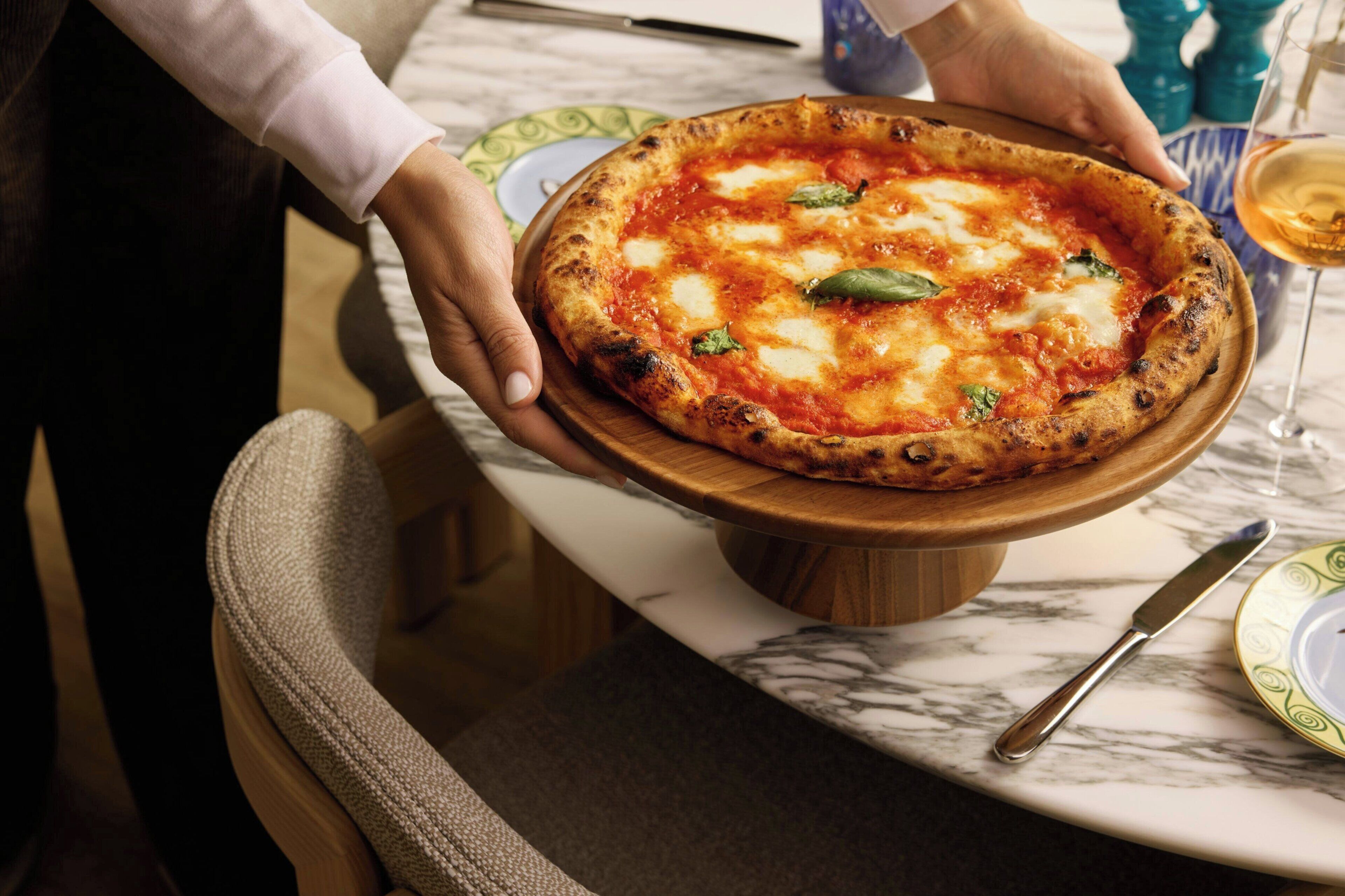 Une personne tenant une pizza sur une planche en bois.