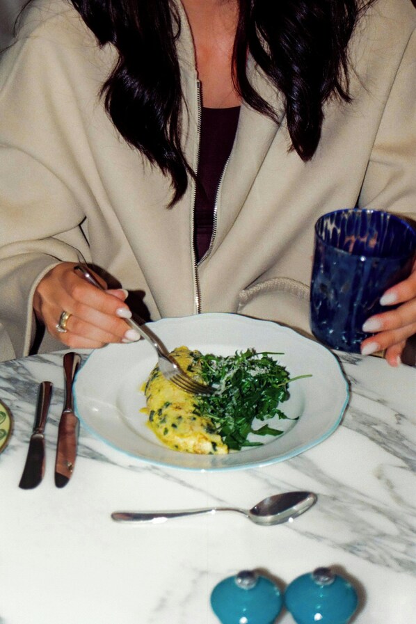A person dining with a plate of food, cutlery, and a blue glass cup on a marble table. - Principessa Forte dei Marmi, Autograph Collection (Forte dei Marmi)