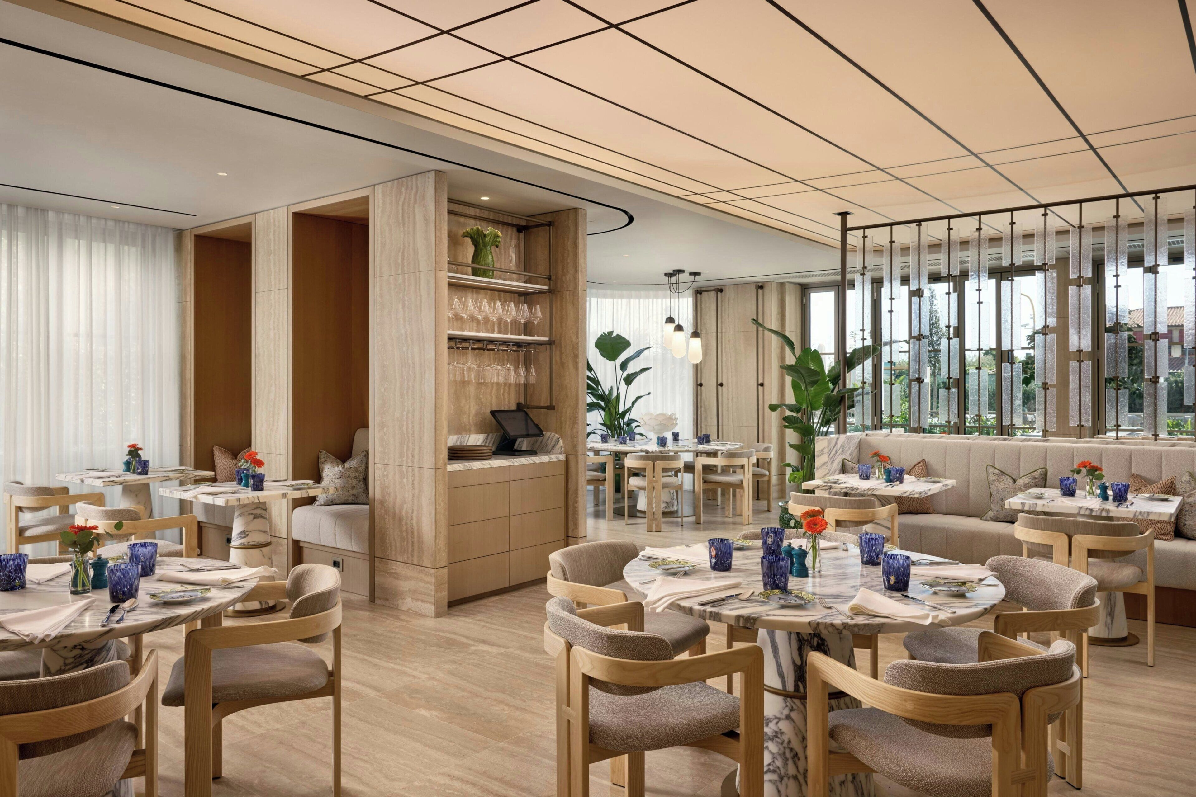 A modern dining area with wooden furniture, marble tables, and a view of the outdoors.