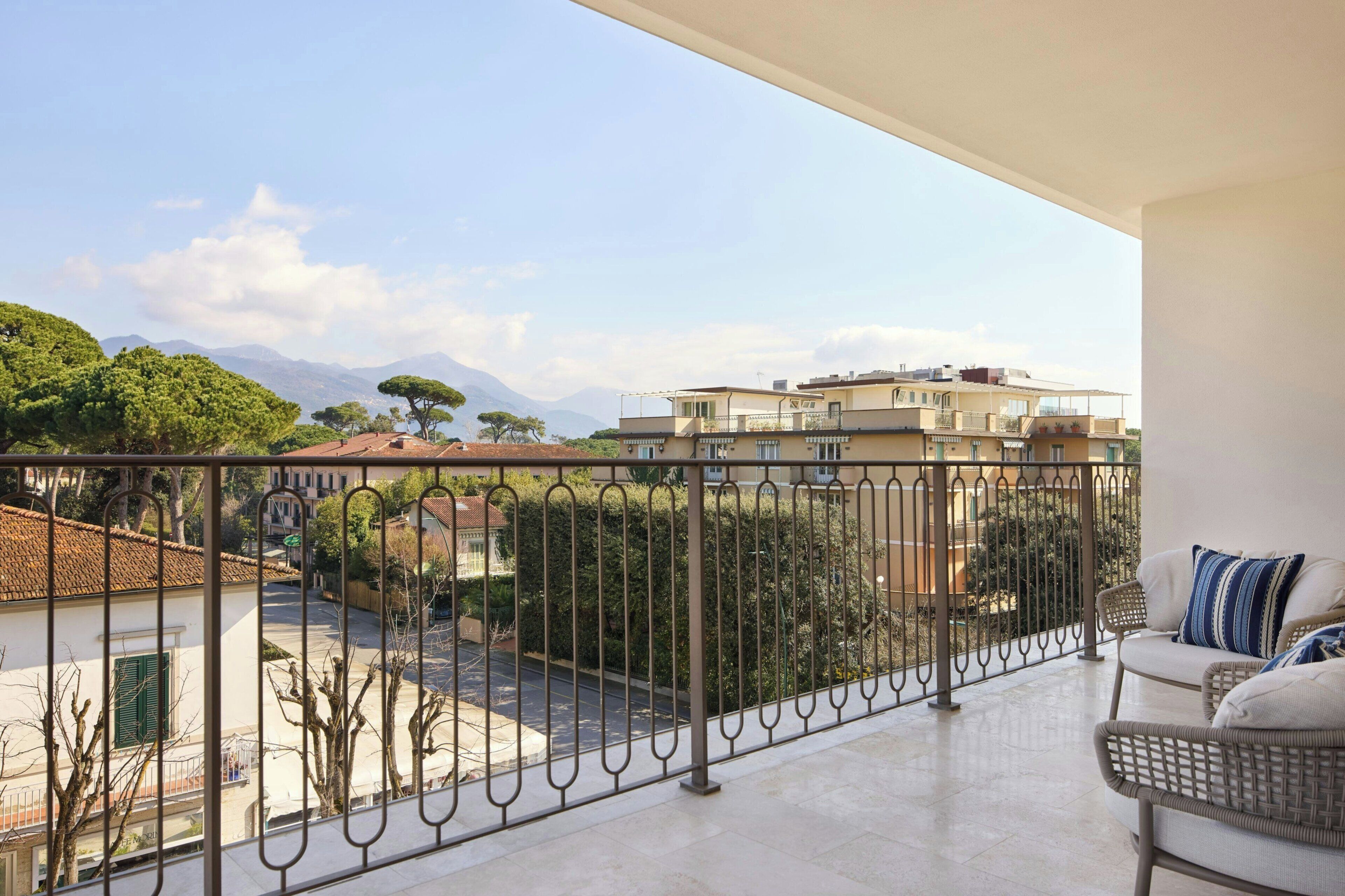 A balcony with a view of a street, buildings, and mountains.