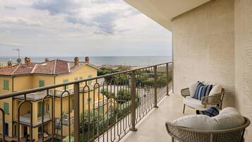 A balcony with a view of a coastal town, a wicker chair, and a railing.