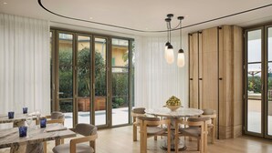 A modern dining area with a round table, multiple chairs, and a view through large glass doors to an outdoor space. - Principessa Forte dei Marmi, Autograph Collection (Forte dei Marmi)