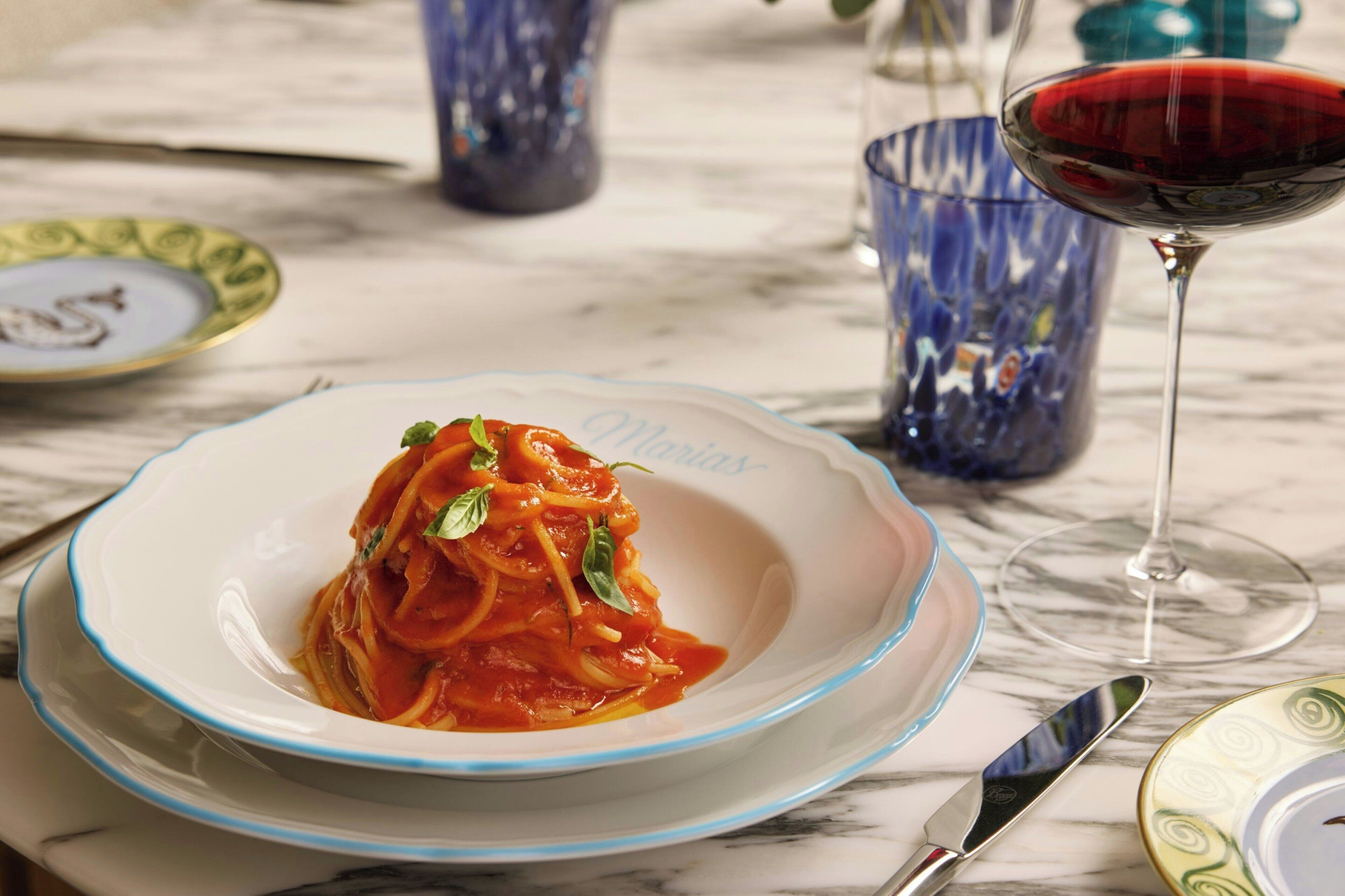 A plate of spaghetti with a red sauce and basil garnish on a white plate with a blue rim, placed on a marble table.