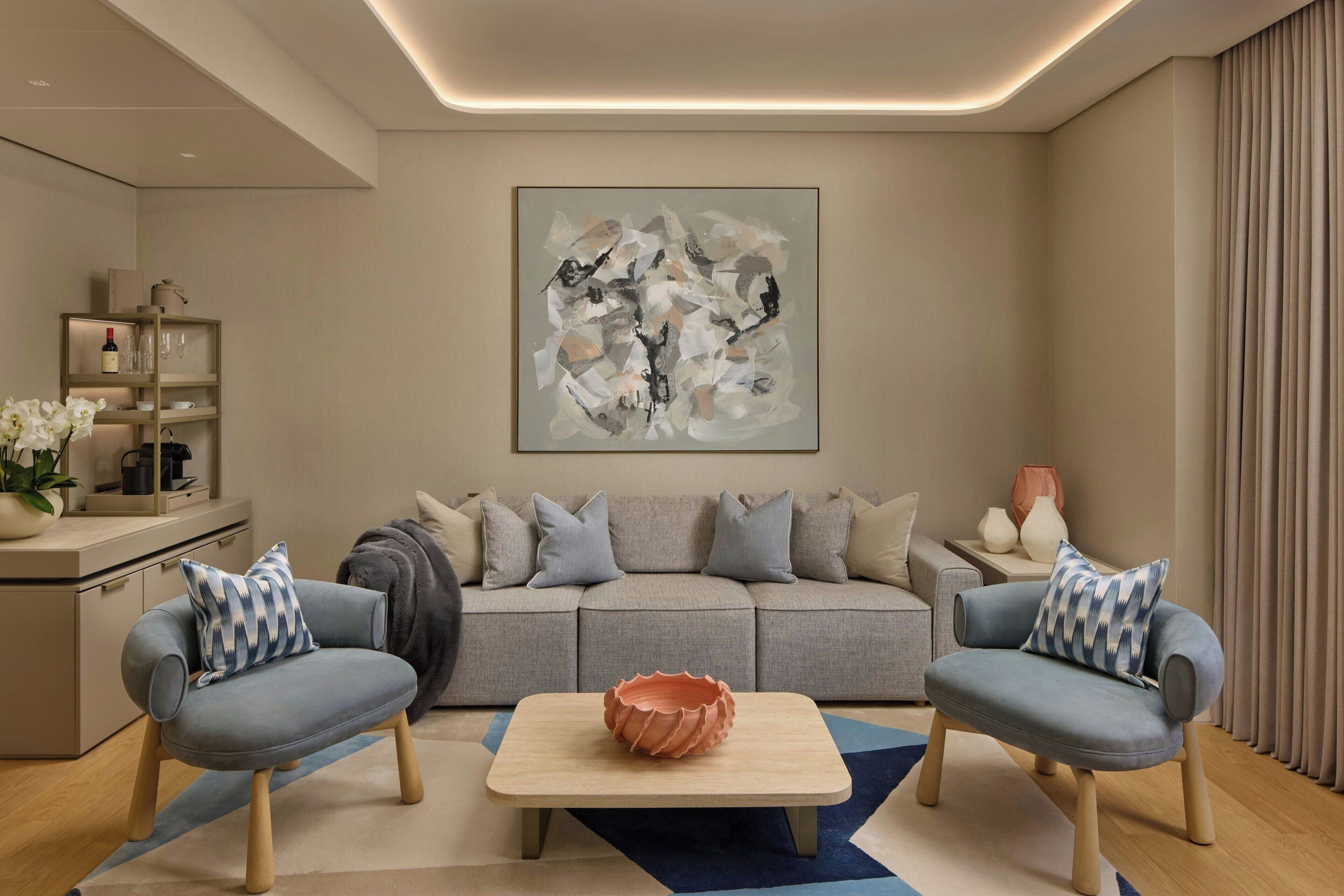 A modern living room with a grey sofa, two armchairs, a coffee table, and a large abstract painting on the wall.