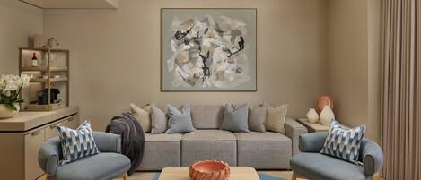 A modern living room with a grey sofa, two armchairs, a coffee table, and a large abstract painting on the wall.