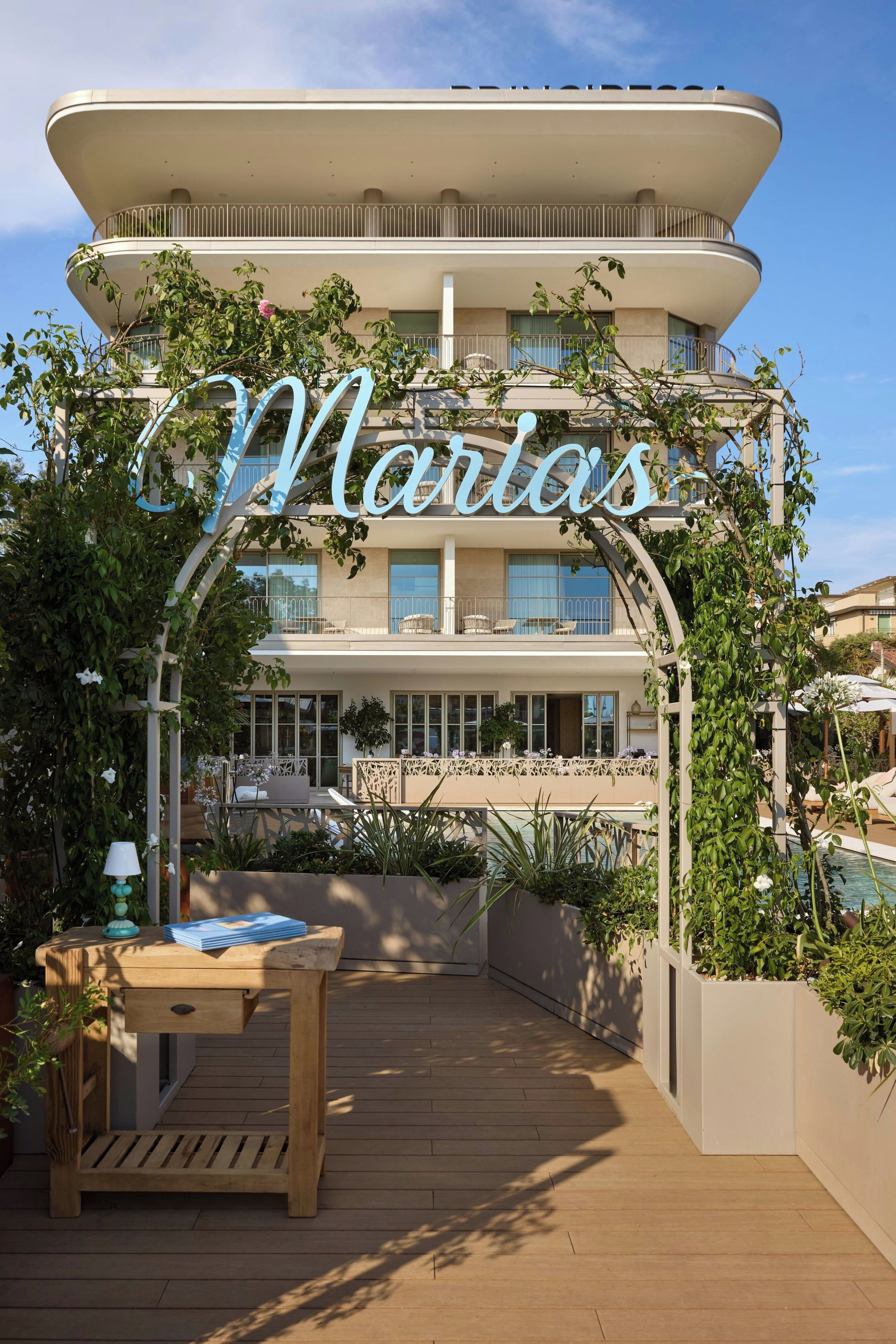 Un hotel de varios pisos con un llamativo letrero 'Marlas', mobiliario exterior y una zona de piscina.