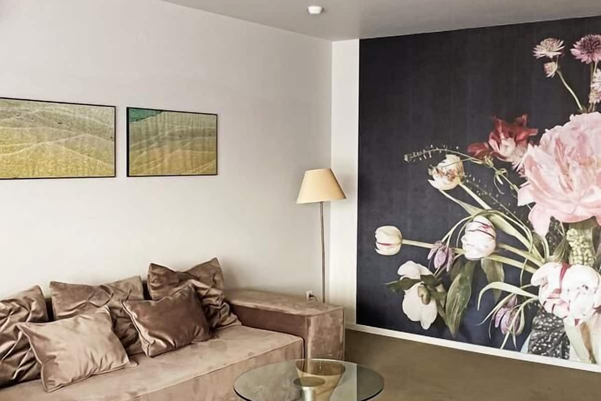 A modern living room with a beige sofa, a glass coffee table, and a large floral painting on the wall.