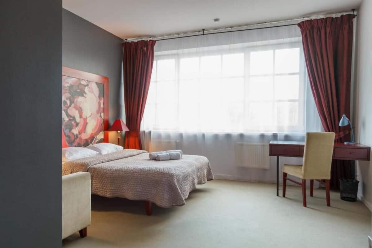 A hotel room with two beds, a desk, a chair, and a large window with curtains.
