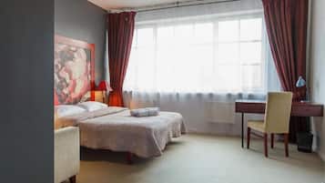 A hotel room with two beds, a desk, a chair, and a large window with curtains.