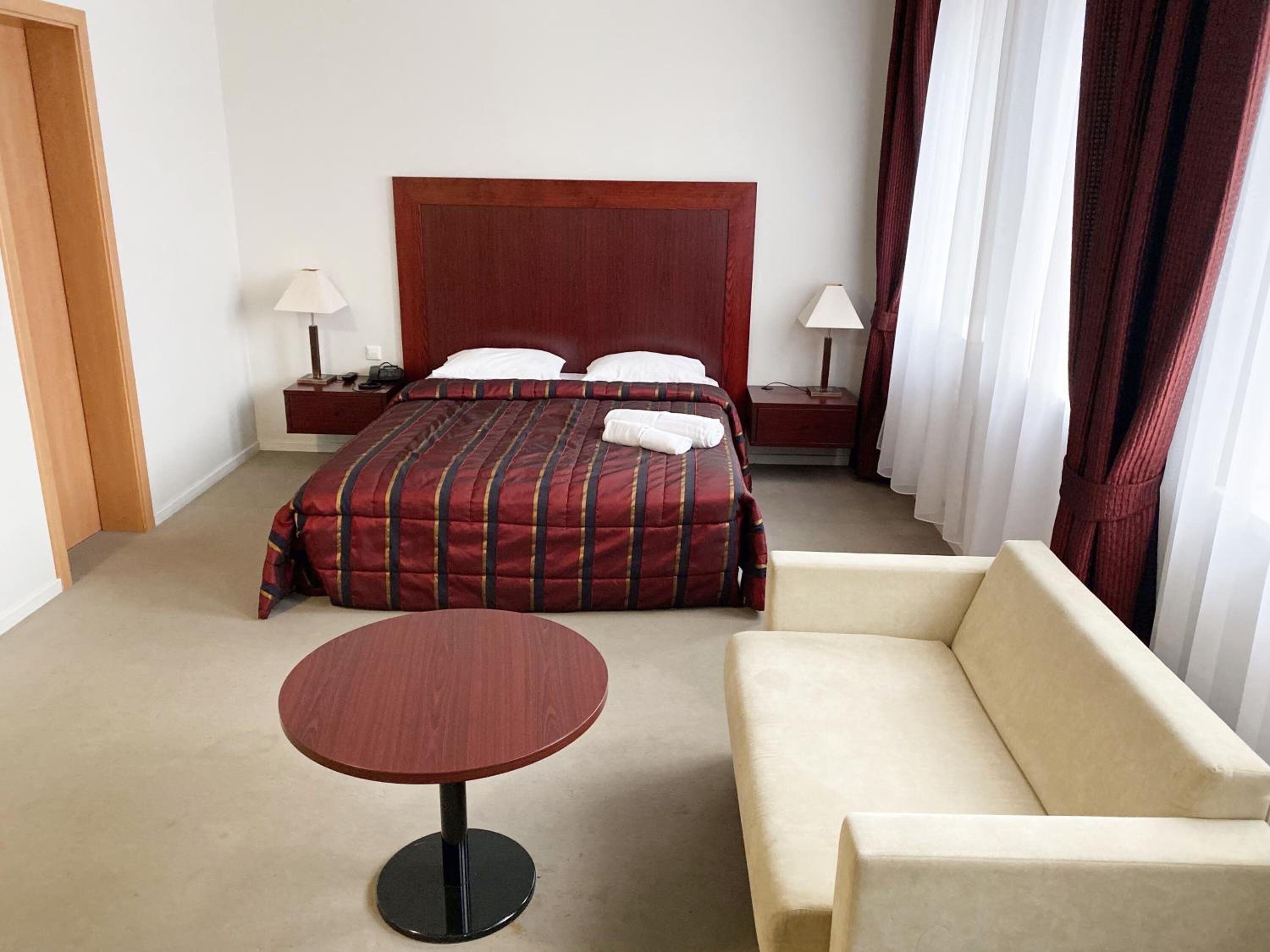 Habitació d'hotel amb un llit gran, dues taules de nit amb làmpades, una taula rodona i un sofà.