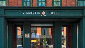 The entrance of the Viesbutis Hotel with a prominent sign, large windows, and flags.