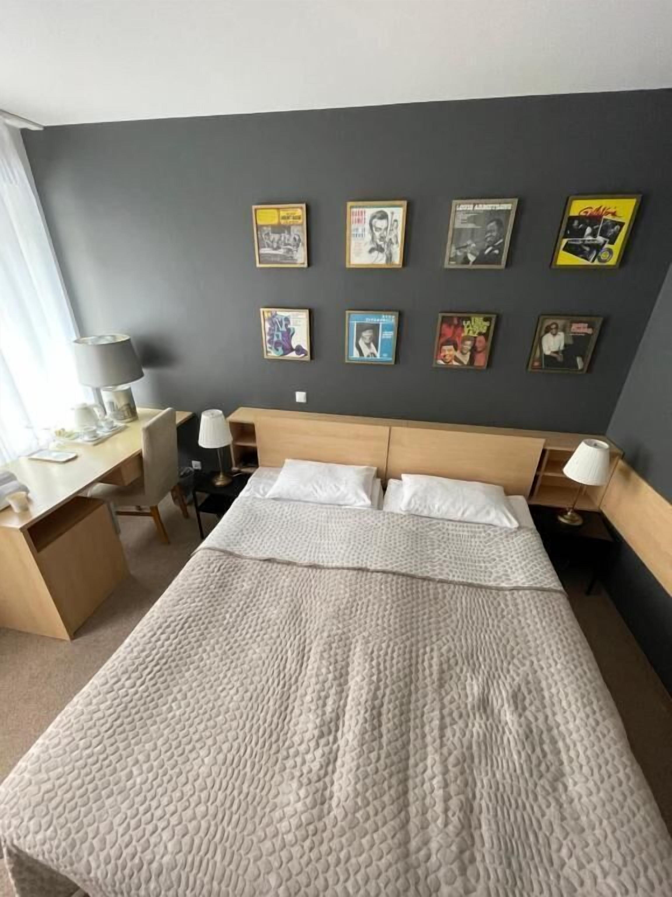 Una habitación de hotel con una cama, un escritorio y una silla. Hay cuadros en la pared.
