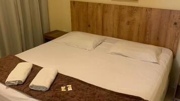 Cama bem arrumada com lençóis brancos e manta marrom, cabeceira de madeira e quadro pendurado na parede.