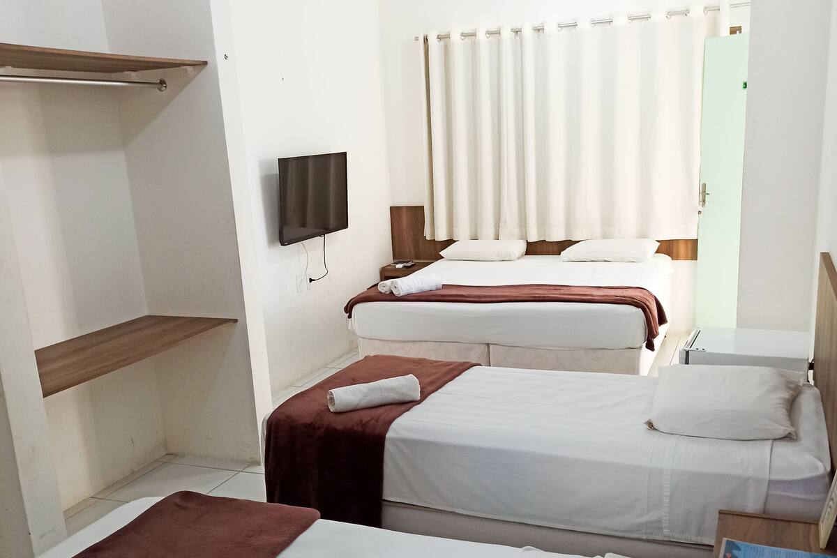 A hotel room with three beds, a TV, and a shower area.