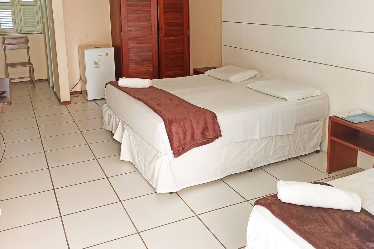 A bedroom with a bed, a wardrobe, a small table, and a refrigerator.