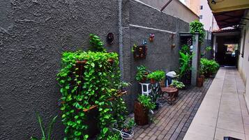 A narrow outdoor corridor with a tiled floor, potted plants, a bicycle, and a bench.