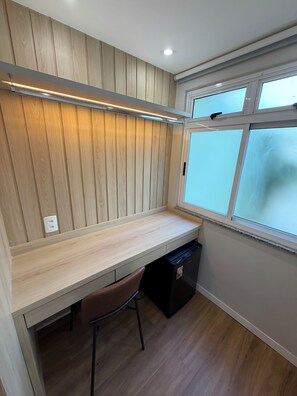 A compact room with a built-in desk, a chair, a black appliance, and a window with frosted glass. - Hotel Cantareira (Niteroi)