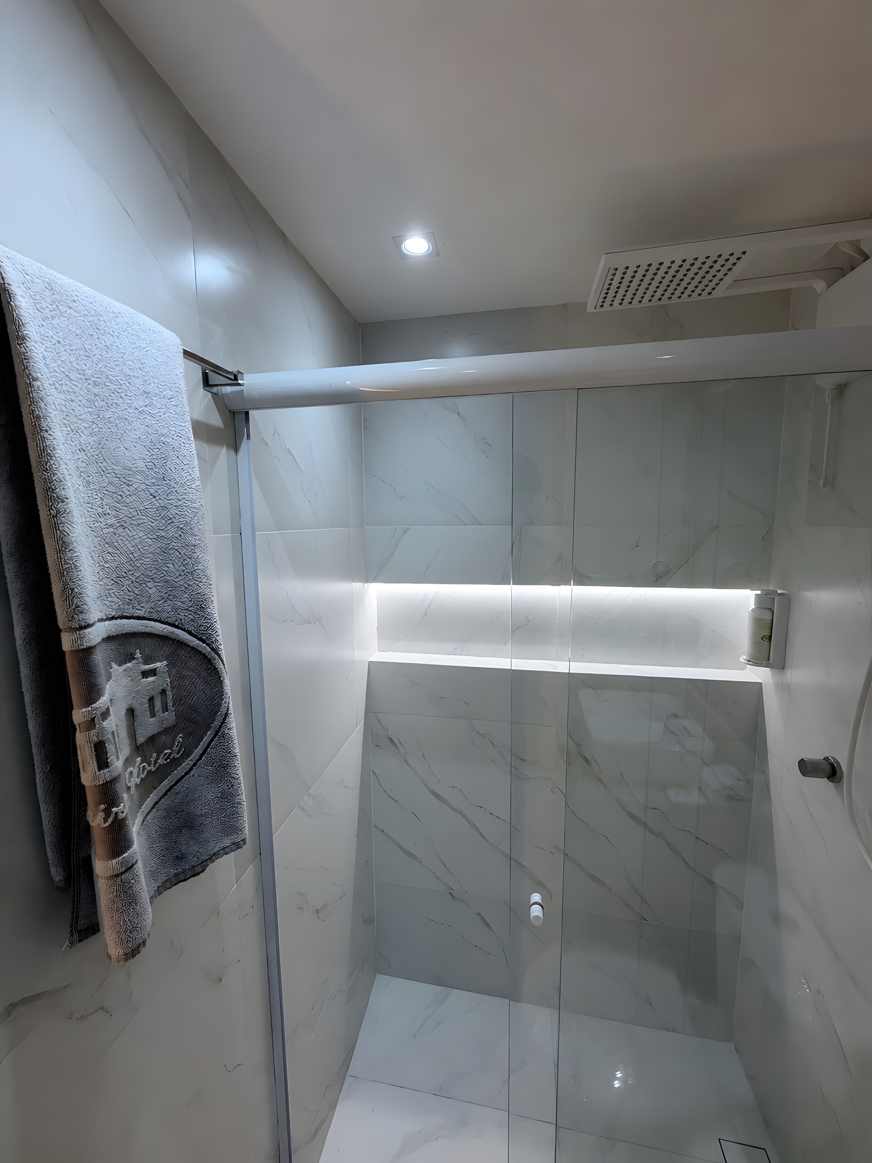 A modern bathroom with a glass shower enclosure, marble tiles, and a towel with a building logo.