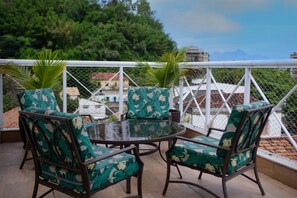 A balcony with a round glass table and four chairs with floral upholstery. - Hotel Cantareira (Niteroi)