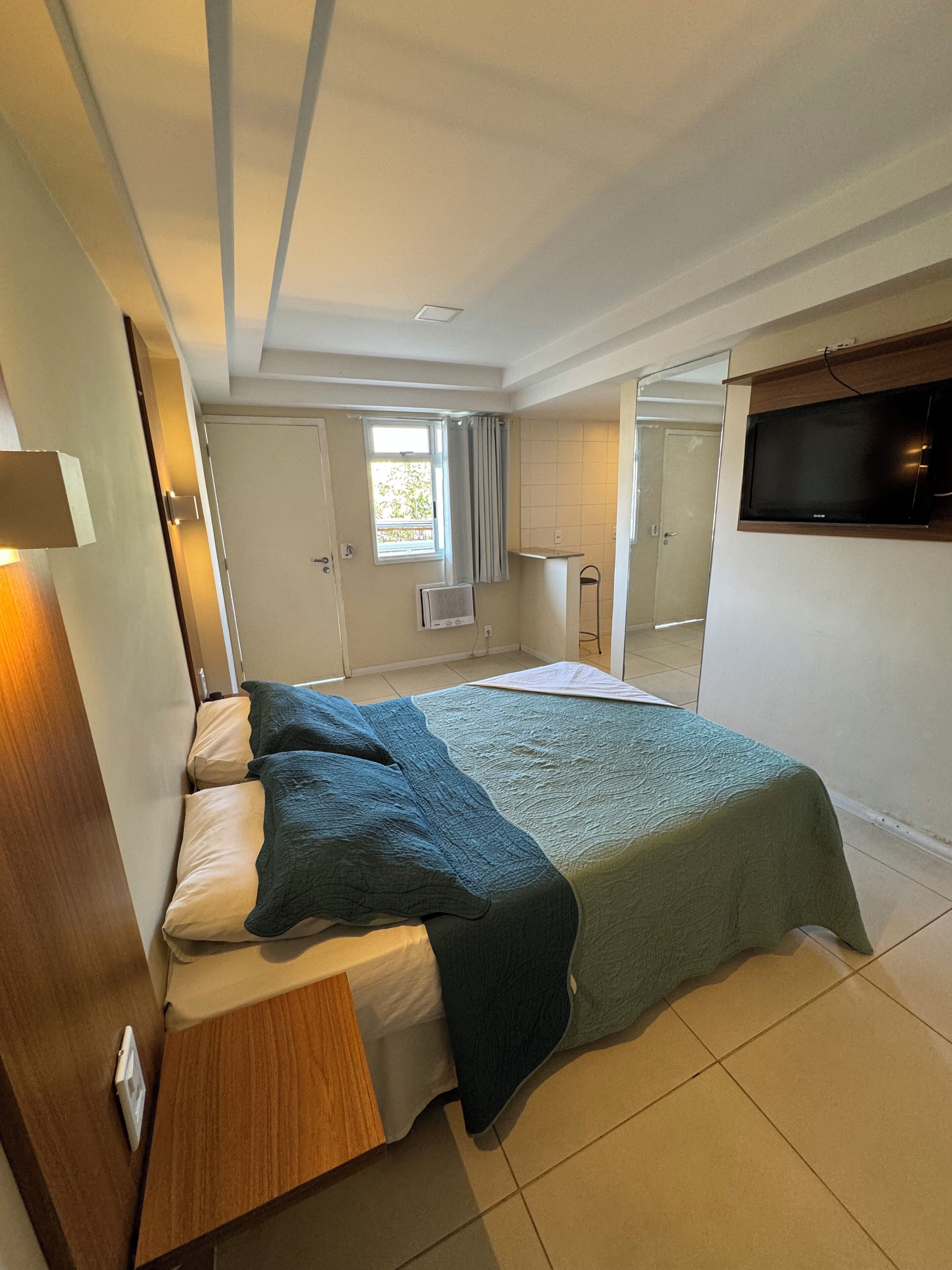 A bedroom with a bed, a TV mounted on the wall, and a window with curtains.