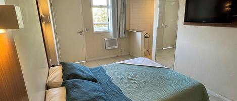 A bedroom with a bed, a TV mounted on the wall, and a window with curtains.