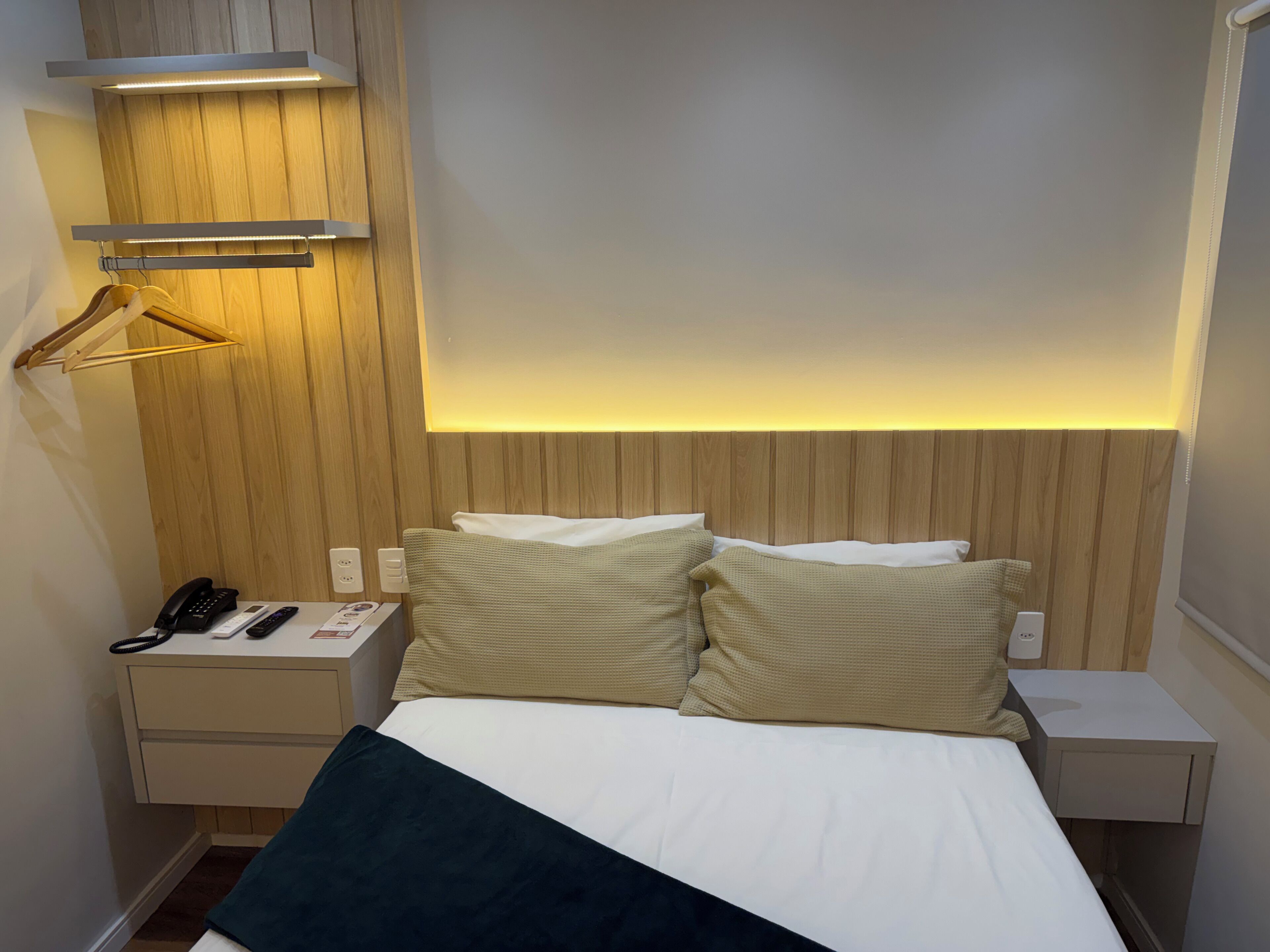 A hotel room with a bed, bedside tables, a telephone, and a lighted wall panel.