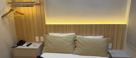 A hotel room with a bed, bedside tables, a telephone, and a lighted wall panel.