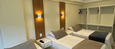 Habitación de hotel con tres camas individuales, cada una con almohada y manta. Hay mesitas de noche con lámparas y teléfono. La habitación tiene un revestimiento de pared de madera y un espejo grande sobre las camas.