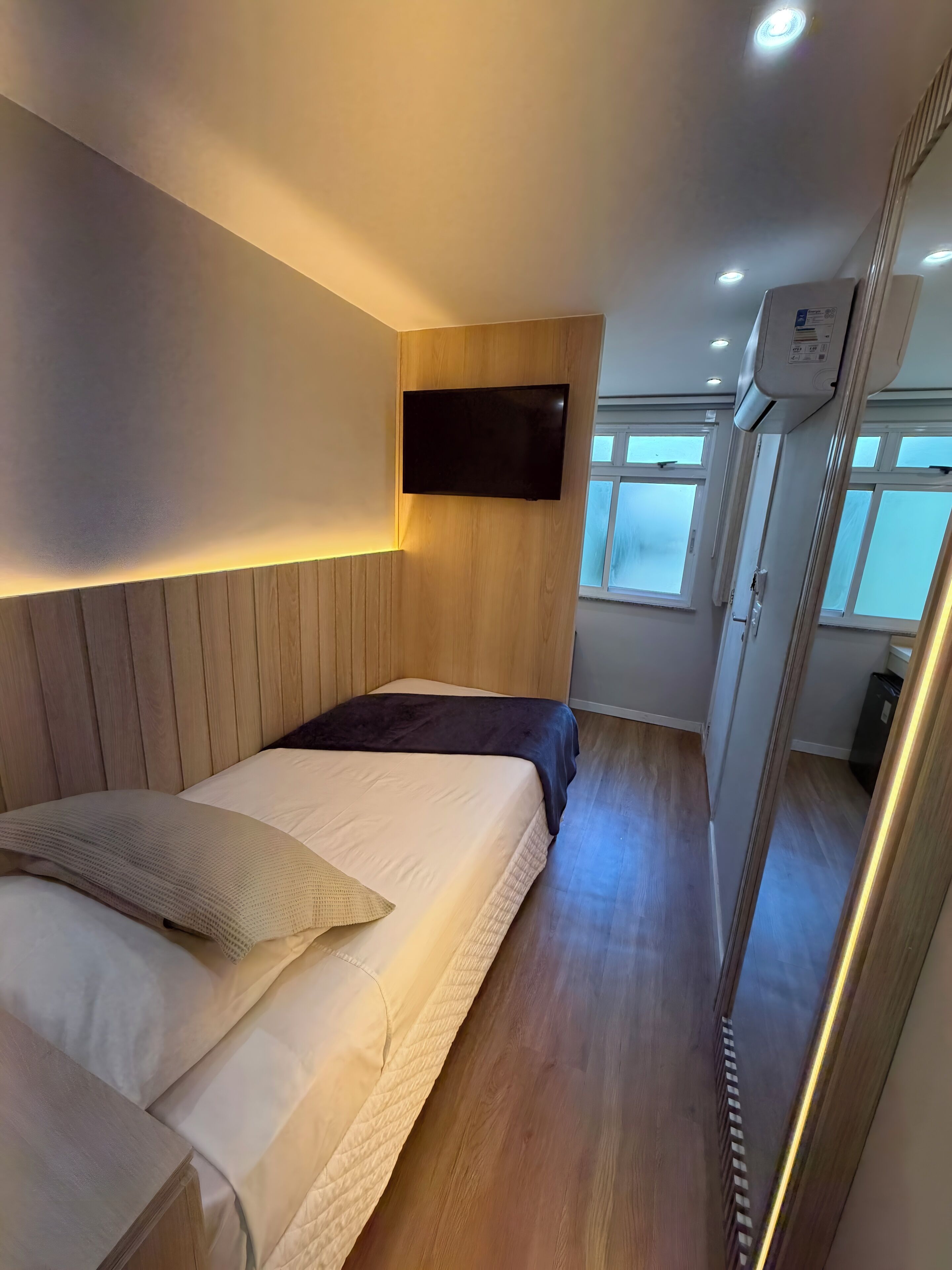 A bedroom with a bed, a mounted TV, and a window.