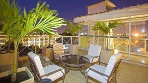 Terraza en la azotea con mobiliario exterior, palmeras y una estructura de vidrio.