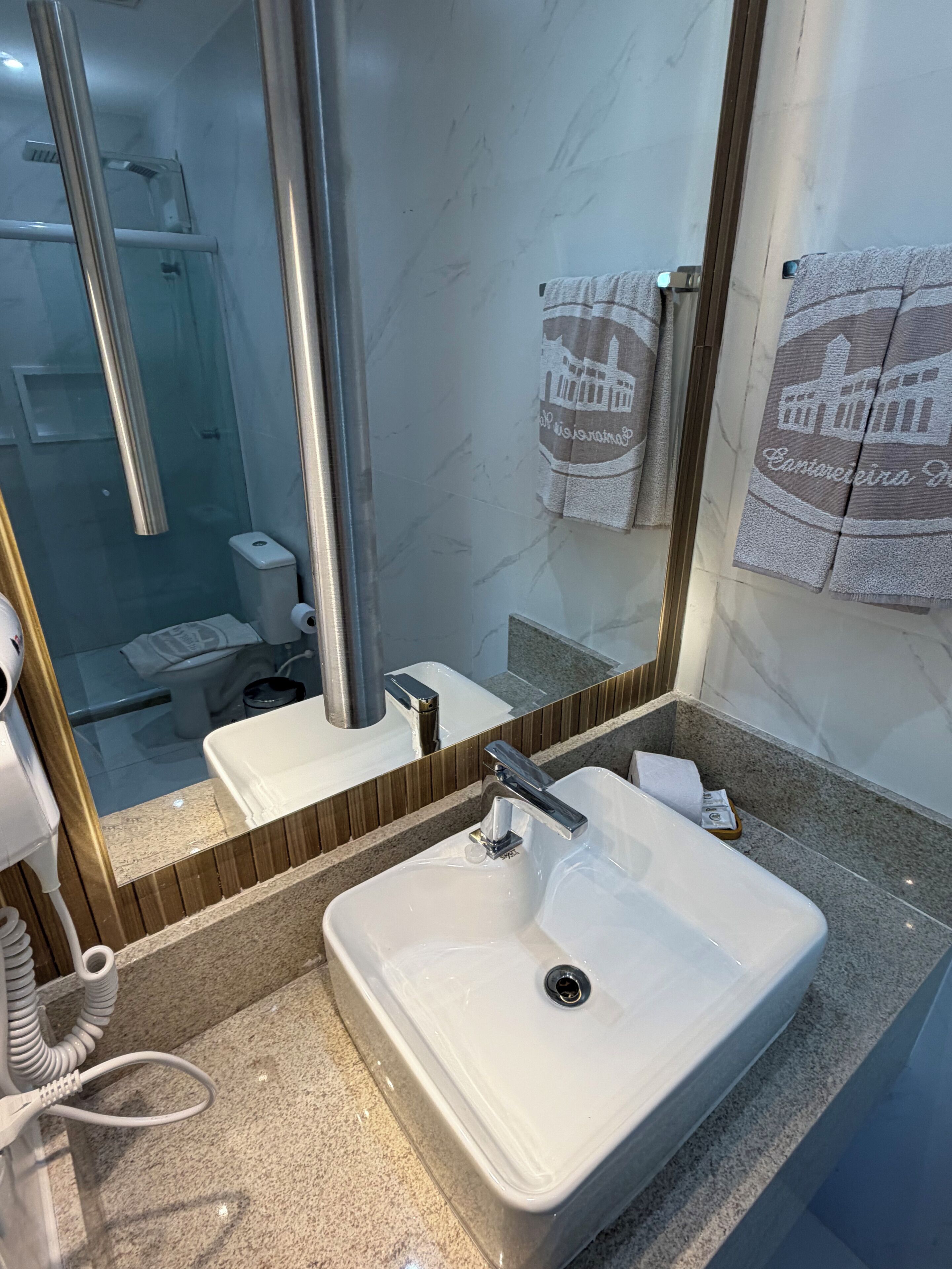 Un baño con lavamanos blanco, un espejo y un perchero con toallas.